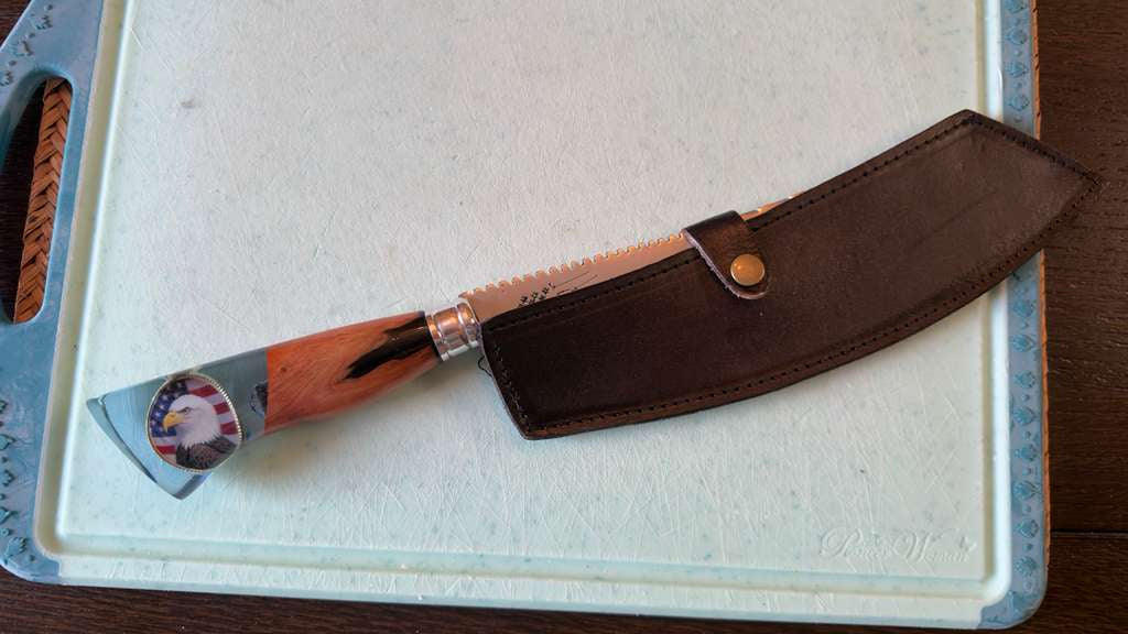 Knife with a wooden handle and leather sheath on a cutting board